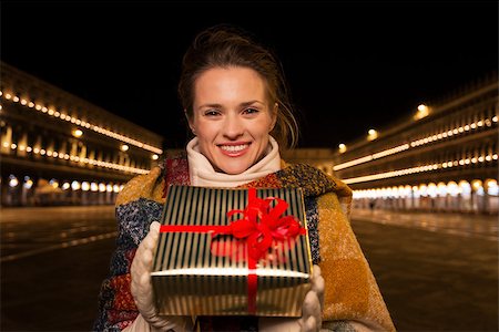 simsearch:400-08344334,k - Excitement of Christmas time and allure of long-time favourite Venice, Italy. Portrait of happy woman holding Christmas gift box while standing on Piazza San Marco in the evening Stock Photo - Budget Royalty-Free & Subscription, Code: 400-08343472
