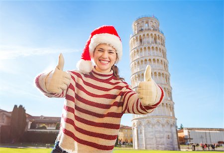 simsearch:400-08344334,k - Young, itching from energy and searching for excitement. I'm going to Christmas trip to Italy. It is a no-brainer. Smiling woman in Santa hat showing thumbs up in front of Leaning Tour of Pisa. Stock Photo - Budget Royalty-Free & Subscription, Code: 400-08343846
