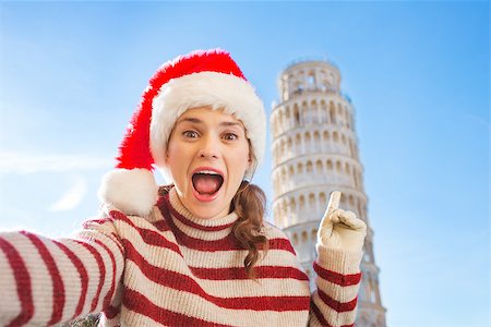 simsearch:400-08344334,k - Young, itching from energy and searching for excitement. I'm going to Christmas trip to Italy. It is a no-brainer. Happy woman in Santa hat taking selfie and pointing on Leaning Tour of Pisa. Stock Photo - Budget Royalty-Free & Subscription, Code: 400-08343854