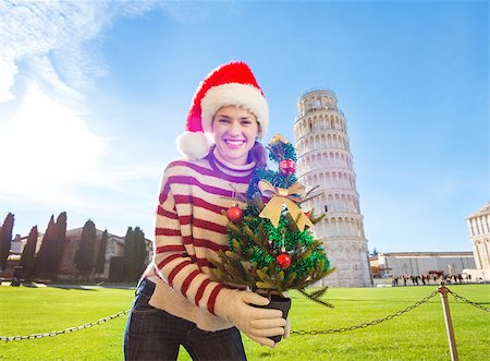simsearch:400-08344334,k - Young, itching from energy and searching for excitement. I'm going to Christmas trip to Italy. It is a no-brainer. Happy woman in Santa hat holding Christmas tree in front of Leaning Tour of Pisa. Stock Photo - Budget Royalty-Free & Subscription, Code: 400-08343856