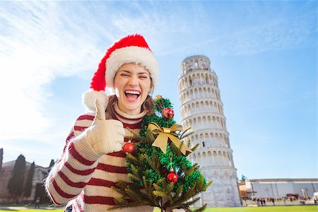 simsearch:400-08344334,k - Young, itching from energy and searching for excitement. I'm going to Christmas trip to Italy. It is a no-brainer. Woman in Santa hat with Christmas tree showing thumbs up near Leaning Tour of Pisa Stock Photo - Budget Royalty-Free & Subscription, Code: 400-08343859