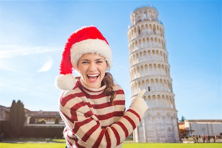 simsearch:400-08344334,k - Young, itching from energy and searching for excitement. I'm going to Christmas trip to Italy. It is a no-brainer. Smiling woman in Santa hat pointing on Leaning Tour of Pisa. Stock Photo - Budget Royalty-Free & Subscription, Code: 400-08343850