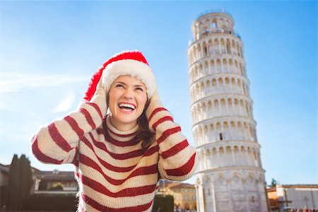 simsearch:400-08344334,k - Young, itching from energy and searching for excitement. I'm going to Christmas trip to Italy. It is a no-brainer. Happy woman in Santa hat looking up on something in front of Leaning Tour of Pisa. Stock Photo - Budget Royalty-Free & Subscription, Code: 400-08343852