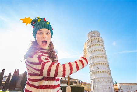 simsearch:400-08344334,k - Young, itching from energy and searching for excitement. I'm going to Christmas trip to Italy. It is a no-brainer. Surprised young woman in Christmas tree hat holding Leaning Tour of Pisa Stock Photo - Budget Royalty-Free & Subscription, Code: 400-08343870