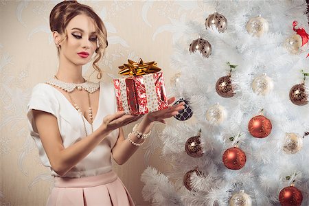 simsearch:400-07218439,k - beautiful brunette woman with elegant fashion outfit, pearl necklace, hair-style and cute make-up taking christmas present in the hand near decorated xmas tree Foto de stock - Super Valor sin royalties y Suscripción, Código: 400-08375480