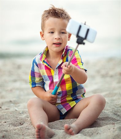 selfie stick - Cute little boy in colorful checkered shirt sitting on the sand and taking picture with smart phone using selfie stick Stock Photo - Budget Royalty-Free & Subscription, Code: 400-08377628