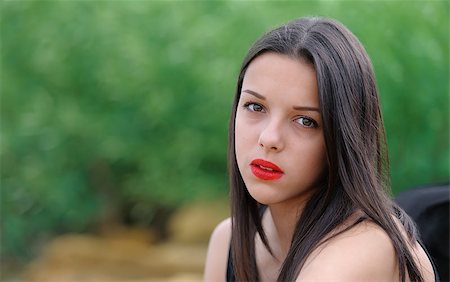 Young beautiful serious brunette girl with red lips and long straight hair over green nature background Stockbilder - Microstock & Abonnement, Bildnummer: 400-08371516