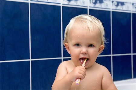 Little girl is brushing teeth in bathroom. Blue tiles behind. Looking at camera Stock Photo - Budget Royalty-Free & Subscription, Code: 400-08373241