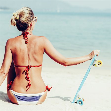 simsearch:400-08400086,k - Suntanned lady in blue and white striped bikini sits on sandy beach and holding her penny board Stock Photo - Budget Royalty-Free & Subscription, Code: 400-08400085