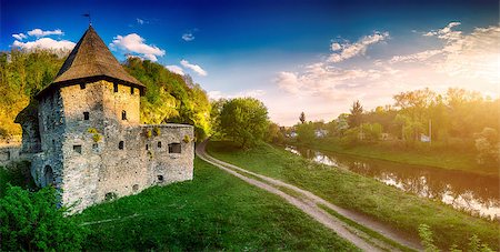 Ancient stone castle in Kamianets Podilskyi standing on hill with green trees and bushes with rural road and river Stock Photo - Budget Royalty-Free & Subscription, Code: 400-08401055