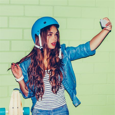simsearch:400-08400085,k - young beautiful long-haired brunette woman in blue helmet taking a selfie self portrait of herself posing with ringlet curl hair at the camera on her smartphone digital camera near the green brick wall Photographie de stock - Aubaine LD & Abonnement, Code: 400-08401385