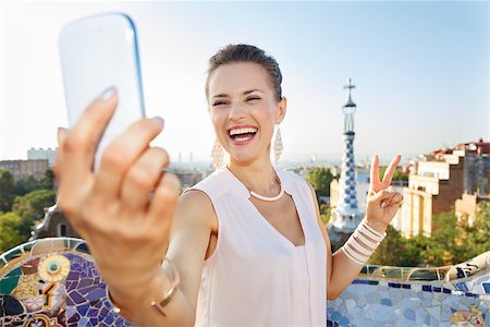 simsearch:400-08415527,k - Refreshing promenade in unique Park Guell style in Barcelona, Spain. Portrait of smiling young woman showing victory gesture and taking selfie with smartphone while in Park Guell, Barcelona, Spain Stock Photo - Budget Royalty-Free & Subscription, Code: 400-08415546