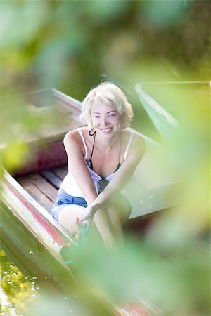 Relaxed young blonde woman  enjoying the sunny summer day on a vintage wooden boats on a lake in pure natural environment on the countryside. Foto de stock - Royalty-Free Super Valor e Assinatura, Número: 400-08426771