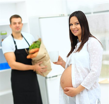 pregnant woman with a cup in her hands turned to her husband, who holds a package with products Photographie de stock - Aubaine LD & Abonnement, Code: 400-08428794