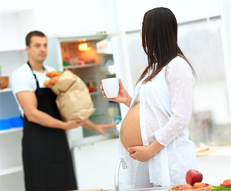 pregnant woman with a cup in her hands turned to her husband, who holds a package with products Photographie de stock - Aubaine LD & Abonnement, Code: 400-08428795