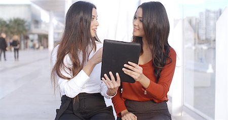 Two women sitting outdoors on a high key urban esplanade discussing information on a tablet computer which they are both holding Stock Photo - Budget Royalty-Free & Subscription, Code: 400-08431087
