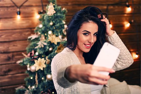 people, holidays and technology concept - beautiful brunette woman in white Christmas sweater taking selfie picture by smartphone over christmas tree living room background Foto de stock - Super Valor sin royalties y Suscripción, Código: 400-08431923