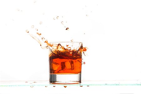 View of whiskey glass with ice cubes and drink splash on white background. Foto de stock - Royalty-Free Super Valor e Assinatura, Número: 400-08432187