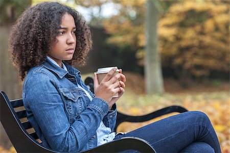 Beautiful mixed race African American girl teenager female young woman drinking takeaway coffee outside sitting on a park bench in autumn or fall looking sad depressed or thoughtful Stock Photo - Budget Royalty-Free & Subscription, Code: 400-08432868