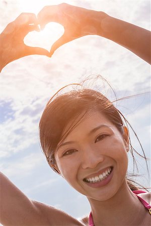 simsearch:400-08291180,k - Beautiful young smiling Chinese Asian woman girl on a beach in a bikini, making a hand heart shaped finger frame Foto de stock - Royalty-Free Super Valor e Assinatura, Número: 400-08433188