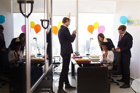 Business woman celebrating birthday and doing a party with colleagues in her office. A friend with mobile phone takes pictures of her blowing out clandles on birthday cake. Wide shot Stock Photo - Budget Royalty-Free & Subscription, Code: 400-08433257