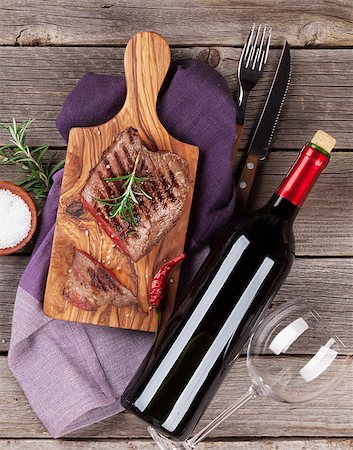 Grilled beef steak with rosemary, salt and pepper and wine bottle on wooden table. Top view Foto de stock - Super Valor sin royalties y Suscripción, Código: 400-08495315
