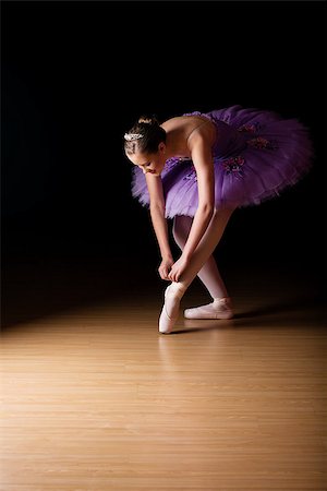 simsearch:400-08496646,k - Young female ballerina wearing a lilac colored tut adjusting her shoes against black background Stockbilder - Microstock & Abonnement, Bildnummer: 400-08496645