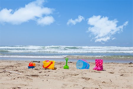 Colorful plastic toys lying on the beach sand with the sea and clouds in the background Stock Photo - Budget Royalty-Free & Subscription, Code: 400-08496642
