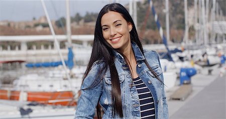 Fun attractive woman smiling at the camera as she enjoys a relaxing day outdoors walking along a waterfront promenade at the marina Stock Photo - Budget Royalty-Free & Subscription, Code: 400-08497527