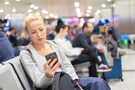 Casual blond young woman using her cell phone while waiting to board a plane at the departure gates. Wireless network hotspot enabling people to access internet conection. Public transport. Stock Photo - Budget Royalty-Free & Subscription, Code: 400-08532580