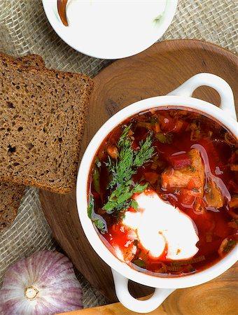 rote-beete-suppe - Traditional Soup Borscht with Beet, Vegetables and Meat. Top View of Borscht in Bowl closeup on Wooden Plate with Brown Bread, Garlic and Sour Cream Stockbilder - Microstock & Abonnement, Bildnummer: 400-08574891