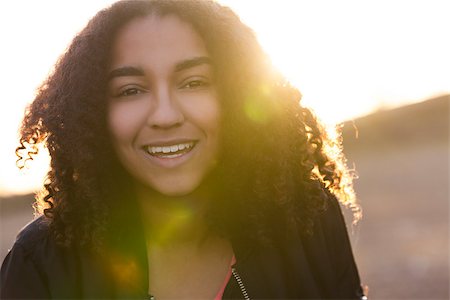 simsearch:400-04068097,k - Beautiful happy mixed race African American girl teenager female young woman with perfect teeth smiling in golden light with sun flare at sunset or sunrise Stockbilder - Microstock & Abonnement, Bildnummer: 400-08572976