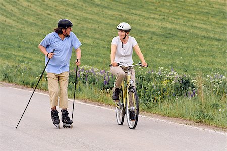 simsearch:400-04609585,k - Senior couple vigorously exercising. The man is Nordic inline skating, and the woman is cycling. They're on a country road through green fields. Stock Photo - Budget Royalty-Free & Subscription, Code: 400-08615446