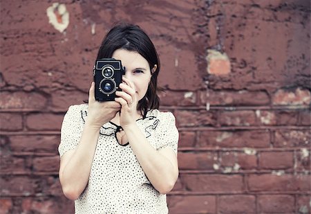 simsearch:614-06895809,k - Girl holding retro camera and taking photo on vintage brick wall background. Selective focus on camera and hands of model. Toned photo with copy space. Vintage style photo. Stock Photo - Budget Royalty-Free & Subscription, Code: 400-08626493