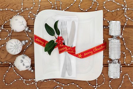 red ribbon and plant - Christmas dinner table setting with white porcelain square plate, knife and fork, linen serviette, red merry christmas  ribbon, silver bauble decorations and cracker over oak background. Stock Photo - Budget Royalty-Free & Subscription, Code: 400-08627931
