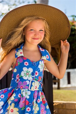 simsearch:400-04140663,k - Outdoor portrait of beautiful girl in blue floral dress and beach straw hat. She holds her big hat and smile to camera. Summer sunny day. House with wooden fence at tropical background. Mothers day. Photographie de stock - Aubaine LD & Abonnement, Code: 400-08620899