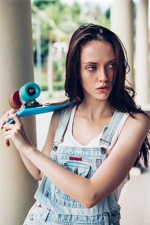 Closeup portrait of sexy beautiful woman in white t-shirt and short denim overall holding blue short skate board. Urban scene, city life. Cute attractive sexy hipster lady standing in front of column. Stock Photo - Budget Royalty-Free & Subscription, Code: 400-08622331