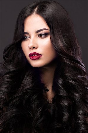 Beautiful brunette model with curls, classic makeup and red lips. The beauty of the face. Portrait shot in the studio on a gray background. Photographie de stock - Aubaine LD & Abonnement, Code: 400-08623145