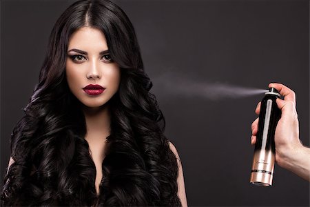 simsearch:400-04692629,k - Beautiful brunette model with curls, classic makeup and red lips with a bottle of hair products. The beauty of the face. Portrait shot in the studio on a gray background. Foto de stock - Super Valor sin royalties y Suscripción, Código: 400-08623143