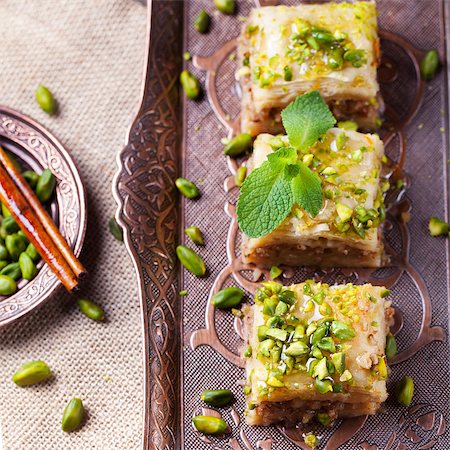 Turkish pistachio and phyllo pastry dessert, baklava on a authentic cooper tray with a plate of pistachios and stick of cinnamon Photographie de stock - Aubaine LD & Abonnement, Code: 400-08669863
