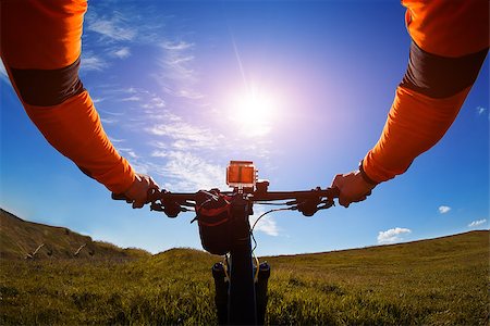 Hands in orange jacket holding handlebar of a bicycle with green meadow on background Stock Photo - Budget Royalty-Free & Subscription, Code: 400-08674304