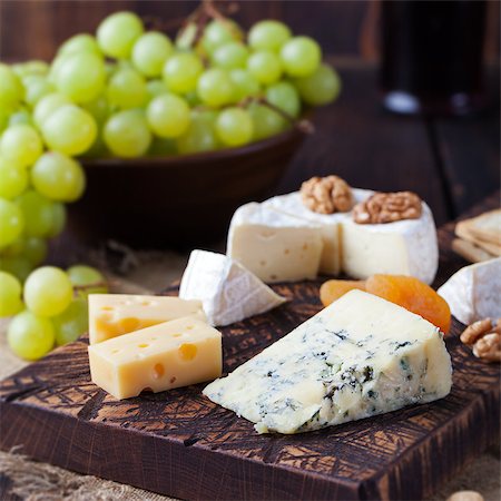 Assortment of cheese with honey, nuts and grape on a rustic cutting board wooden background Foto de stock - Super Valor sin royalties y Suscripción, Código: 400-08670406