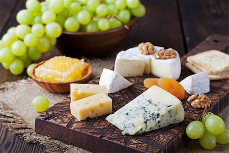 Assortment of cheese with honey, nuts and grape on a rustic cutting board wooden background Foto de stock - Super Valor sin royalties y Suscripción, Código: 400-08670407