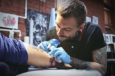 Beautiful tattooist with tunnels makes a tattoo on his leg Fotografie stock - Microstock e Abbonamento, Codice: 400-08671561