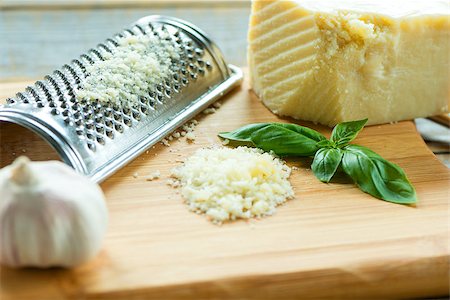 Heap of grated Parmesan on wooden background with leaf of basilic,garlic and  with grater.Close up shot Foto de stock - Royalty-Free Super Valor e Assinatura, Número: 400-08706154