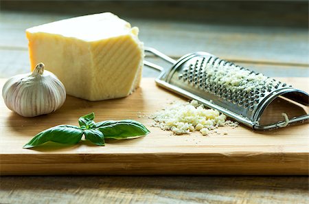 Heap of grated Parmesan on wooden background with leaf of basilic, garlic and  with grater.Close up shot Foto de stock - Royalty-Free Super Valor e Assinatura, Número: 400-08706153