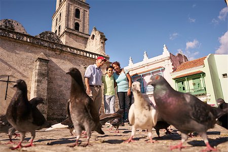 Happy tourists on holiday in Cuba. Hispanic people traveling in Havana. Grandpa and grandson feeding birds, giving food to pigeons in square Stock Photo - Budget Royalty-Free & Subscription, Code: 400-08706429