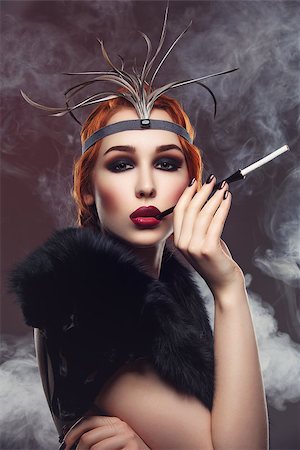 Beautiful young woman with smoky eyes and full red lips holding cigarette holder. Vintage head piece. Retro styling. Studio beauty shot over smoky background. Copy space. Stock Photo - Budget Royalty-Free & Subscription, Code: 400-08735036