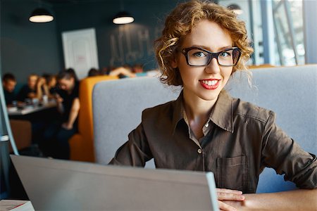 freelancer - joyful smiling woman sitting in a cafe near the open laptop at a table made of wood . in the background a bright window with bright daylight Stock Photo - Budget Royalty-Free & Subscription, Code: 400-08730887