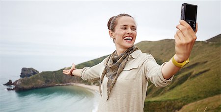 simsearch:400-04969165,k - Into the wild in Spain. smiling active woman hiker taking selfie with digital camera in front of ocean view landscape Stock Photo - Budget Royalty-Free & Subscription, Code: 400-08731577